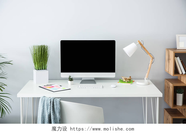 一个白色的桌子上电脑和台灯还有绿色的植被时尚的工作场所, 靠近光墙的现代电脑
